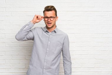 Gözlüklü beyaz tuğla duvar üzerinde Sarışın adam ve şaşırttı