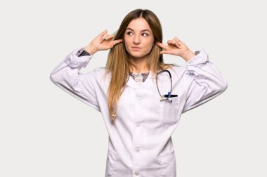 Gri arka planda iki kulağını da tutan genç bir doktor kadın.
