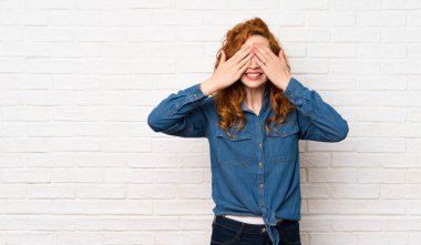 Elleri ile gözleri kaplayan beyaz tuğla duvar üzerinde Redhead kadın
