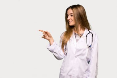 Genç doktor kadın, gri arka planda yan pozisyonu işaret ediyor.