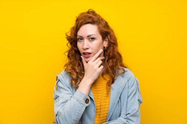 Izole sarı arka plan ayakta ve bir fikir düşünme üzerinde Redhead kadın