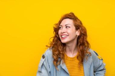 Izole sarı arka plan üzerinde Redhead kadın gülerek ve yukarı bakıyor