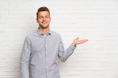 Bir reklam eklemek için avuç üzerinde copyspace hayali tutan beyaz tuğla duvar üzerinde Blonde adam