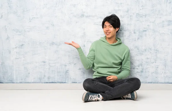 広告を挿入するために手のひらにコピースペースの架空を保持して床に座っているアジアの男性 — ストック写真