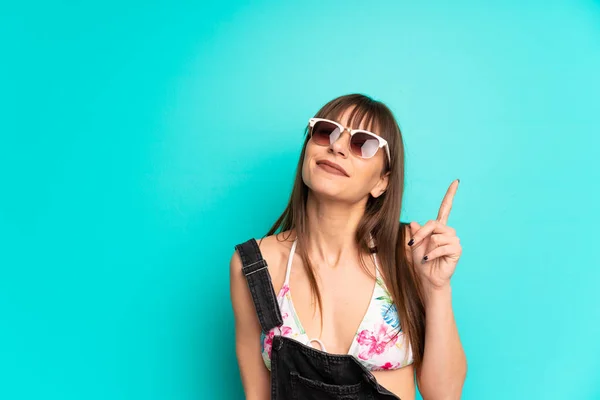 Mavi Duvarın Üstünde Bikinili Genç Bir Kadın Işaret Parmağıyla Işaret — Stok fotoğraf