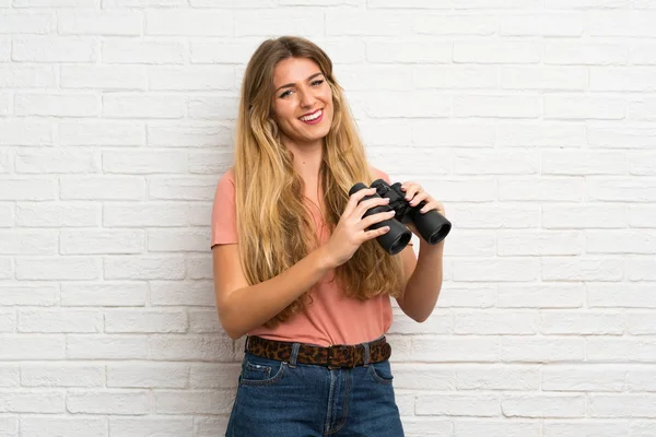 Mujer Rubia Joven Sobre Pared Ladrillo Blanco Con Prismáticos Negros —  Fotos de Stock