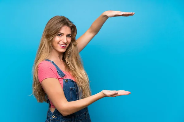 Jonge Blonde Vrouw Met Overalls Geïsoleerde Blauwe Muur Met Copyspace — Stockfoto