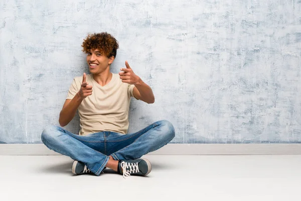Νεαρός Αφροαμερικάνος Κάθεται Στο Πάτωμα Δείχνοντας Προς Εμπρός Και Χαμογελώντας — Φωτογραφία Αρχείου