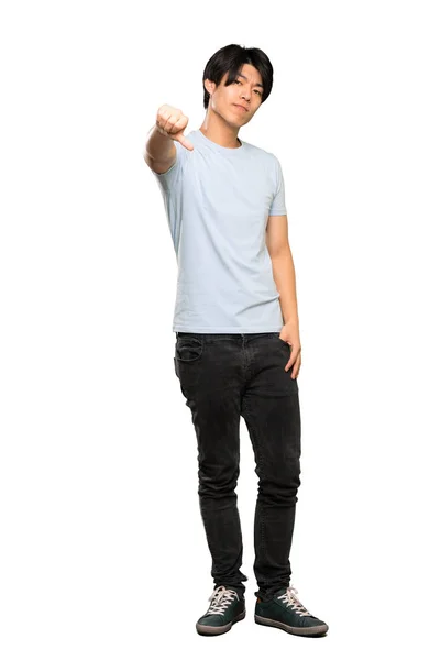 孤立した白い背景の上に否定的な表情で親指を下に示す青いシャツを着たアジア人男性のフルレングスショット — ストック写真