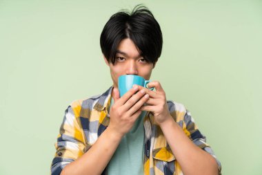 Izole yeşil duvar üzerinde Kahve sıcak fincan tutan Asyalı adam