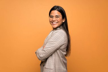 Genç Kolombiyalı kız kahverengi duvarın arkasında kollarını kavuşturup ileriye bakıyor.