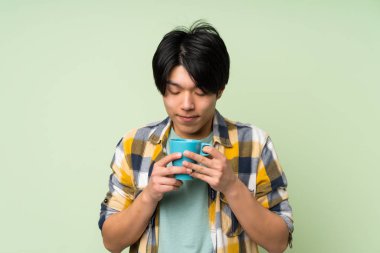 Izole yeşil duvar üzerinde Kahve sıcak fincan tutan Asyalı adam