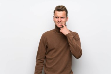 Yukarı bakarken şüpheleri olan izole beyaz duvar üzerinde Blonde adam