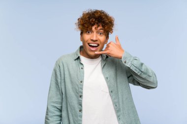 Genç Afro-Amerikan adam izole edilmiş mavi duvarın üzerinde telefon jesti yapıyor. Bana geri dönüş işareti ver.