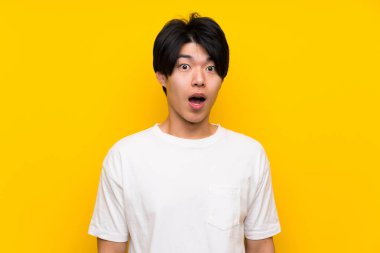 Sürpriz yüz ifadesi ile izole sarı duvar üzerinde Asyalı adam