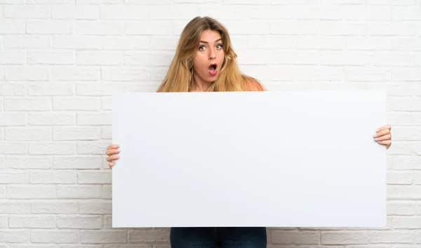 Jovem Loira Sobre Parede Tijolo Branco Segurando Cartaz Branco Vazio — Fotografia de Stock