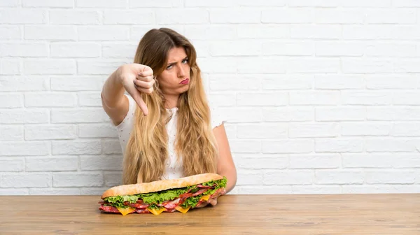 Jovem Loira Segurando Grande Sanduíche Fazendo Mau Sinal — Fotografia de Stock