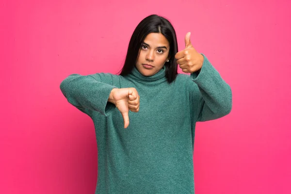 Young Colombian girl with green sweater making good-bad sign. Undecided between yes or not