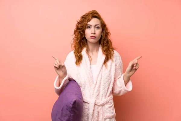 Redhead woman in dressing gown pointing to the laterals having doubts