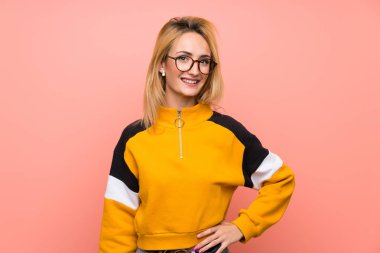 Gözlüklü ve gülümseyen, soyutlanmış pembe arka planı olan genç sarışın kadın.