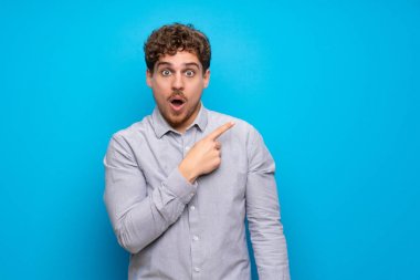 Mavi duvar üzerinde Sarışın adam şaşırttı ve yan işaret