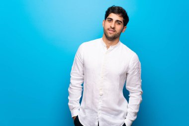 Genç adam mavi duvarın üzerinde mutlu bir ifadeyle