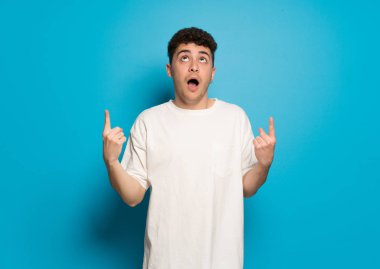 Mavi arka plandaki genç adam şaşırmış ve yukarı bakıyor.