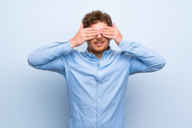 Sarışın adam mavi duvar eller tarafından gözleri kaplama