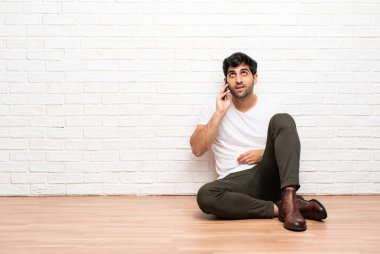 Genç adam yerde oturuyor ve cep telefonuyla konuşuyor.