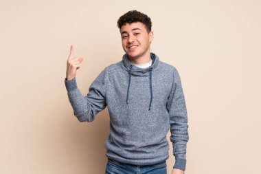 İzole duvar üzerinde genç adam gösteren ve en iyi işareti bir parmak kaldırma