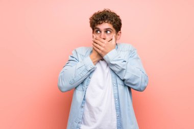 Elleriyle ağız kapsayan pembe duvar üzerinde Sarışın adam