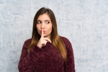 Young girl over grunge wall doing silence gesture