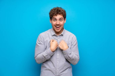 Sarışın adam sürpriz yüz ifadesi ile mavi duvarın üzerinden