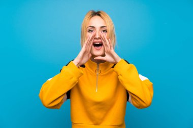 Soyutlanmış mavi arka planda genç sarışın kadın ağzı açık bağırıyor.