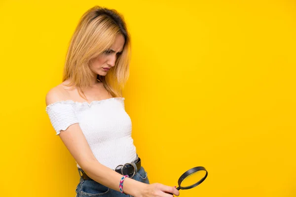 Jonge Blonde Vrouw Geïsoleerde Gele Muur Met Een Vergrootglas — Stockfoto