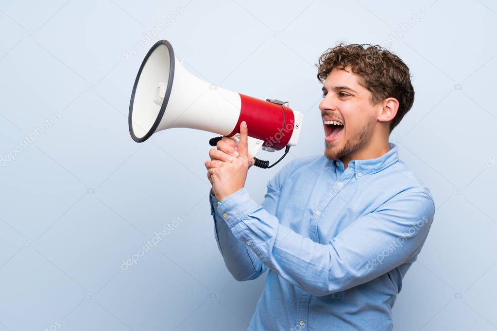 Blonde man over blue wall shouting through a megaphone