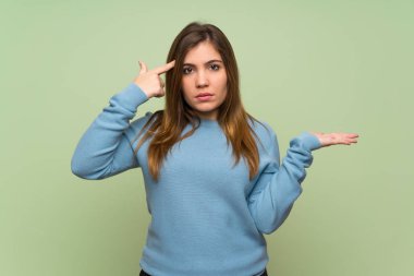 Young girl over green wall making the gesture of madness putting finger on the head
