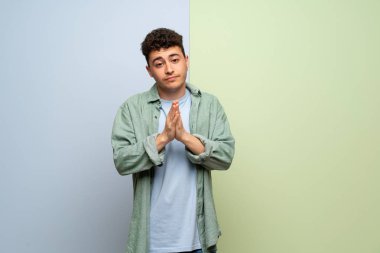 Mavi ve yeşil geçmişi olan genç bir adam avuç içlerini bir arada tutar. İnsan bir şey ister.