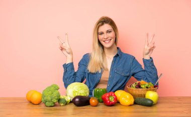 Sebzeli genç sarışın kadın iki eliyle zafer işareti gösteriyor.