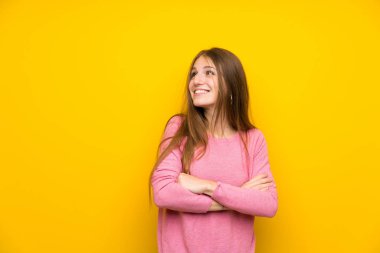 Sarı duvarın üzerinde uzun saçlı genç bir kadın gülümserken yukarı bakıyor.