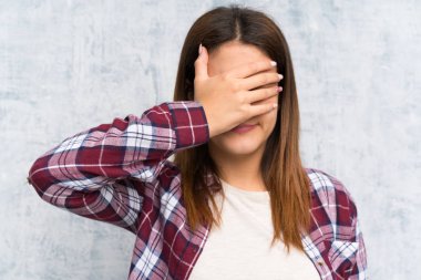 Duvarı örten genç bir kadın elleriyle gözlerini kapatıyor.