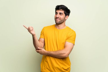 Genç adam pembe duvarın üzerinden parmağını yana doğru gösteriyor.