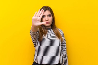 Young girl over yellow wall making stop gesture