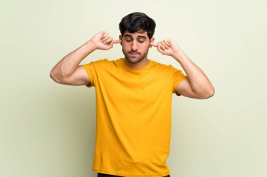 Genç adam pembe duvarın üzerinden iki kulağını da eliyle kapatıyor.