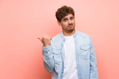 Pembe duvar üzerinde Sarışın adam mutsuz ve yan işaret