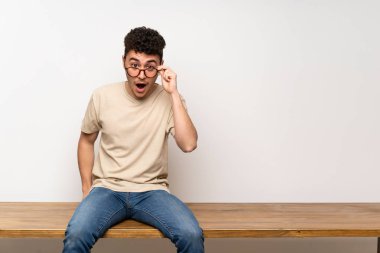 Masada oturan genç adam gözlüklü ve şaşırmış.