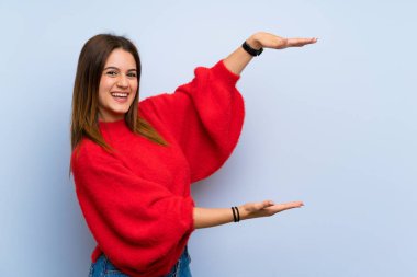 İzole edilmiş mavi duvarın üzerinde ilan vermek için kopyalama alanı tutan genç bir kadın.