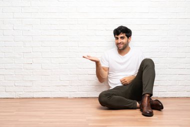 Genç adam yere oturmuş bir fikir sunuyor ve gülümsüyor.