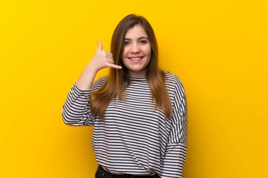 Sarı duvarın üstünde telefon hareketi yapan genç bir kız. Bana geri dönüş işareti ver.