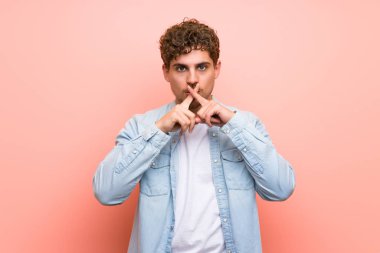 Sessizlik jesti bir işareti gösteren pembe duvar üzerinde Sarışın adam